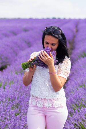 A young brunette woman of European appearance dressed in light casual clothes in a lavender field. Delight in smell and aroma. Lifestyle. Solitude with natureの写真素材