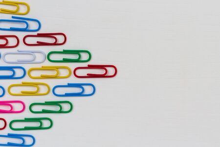 Many multi-colored paper clips form a wedge with place for text on a white wooden table. Background...