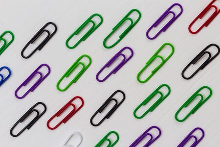 Many multi-colored paper clips lie on a white wooden table. Backgroundの写真素材