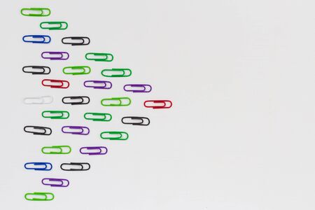 Many multi-colored paper clips form a wedge with place for text on a white wooden table. Background with place for text.の写真素材