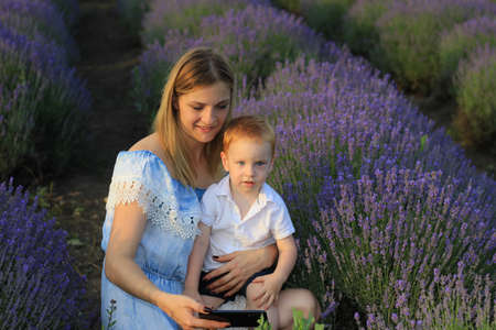 Lifestyle photo shoot of a real family in nature. Mom and son enjoy a stroll through the fresh air and scent on a lavender field in the rays of the setting sun. Selective focus.の写真素材