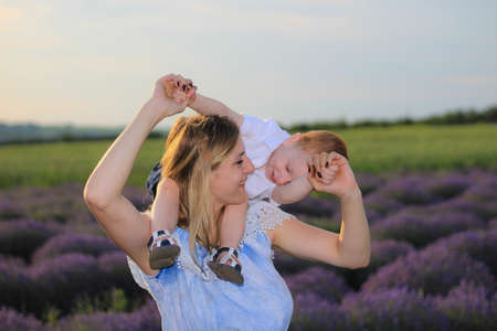 Lifestyle photo shoot of a real family in nature. Mom and son enjoy a stroll through the fresh air and scent on a lavender field in the rays of the setting sun. Selective focus.の写真素材