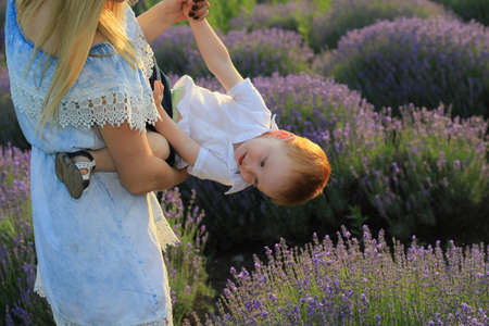 Lifestyle photo shoot of a real family in nature. Mom and son enjoy a stroll through the fresh air and scent on a lavender field in the rays of the setting sun. Selective focus.の写真素材