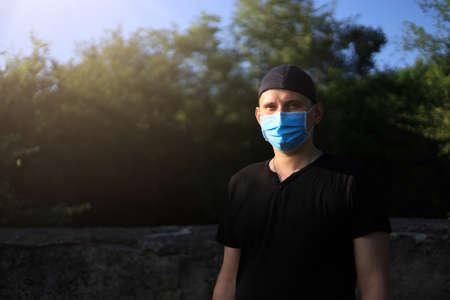 Caucasian young man or adult guy in casual clothes and medical surgical mask enjoys nature outside the city. Toned backgroundの写真素材