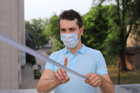 A young man measures out the necessary social distance with a tape measure for life safety during the pandemic of the coronavirus infection Covid-19.の写真素材