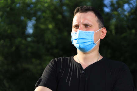 Caucasian young man or adult guy in casual clothes and a medical surgical mask is resting in a city...
