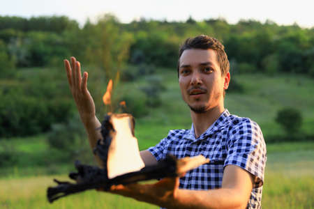 White Caucasian young man or adult guy reading a burning book on blurred forest background. Emotion...