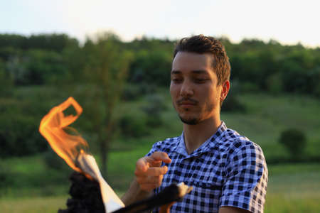 White Caucasian young man or adult guy reading a burning book on blurred forest background.