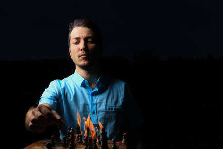 White Caucasian young man or adult guy and a burning chessboard. Dark low key, black background,...