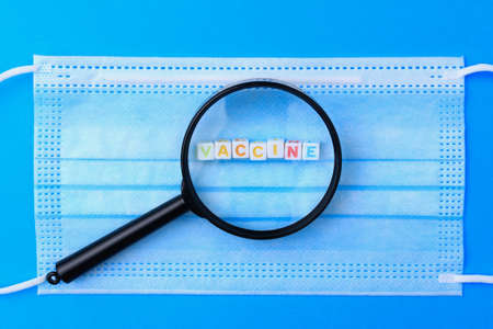 Cubes form the text Vaccine you and a magnifying glass on the background of a medical surgical mask.の写真素材
