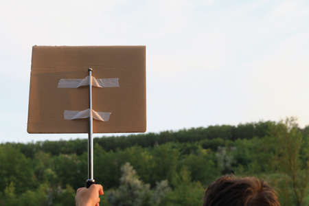 White Caucasian young man or adult guy walks through the park to the city to protest. In his hand he...