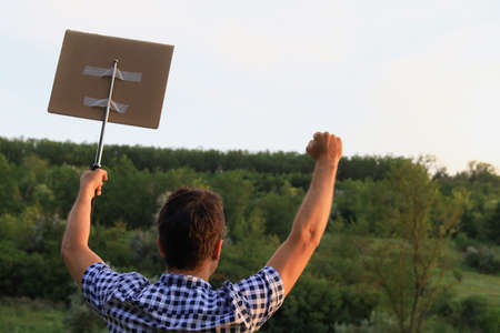 White Caucasian young man or adult guy walks through the park to the city to protest. In his hand he...