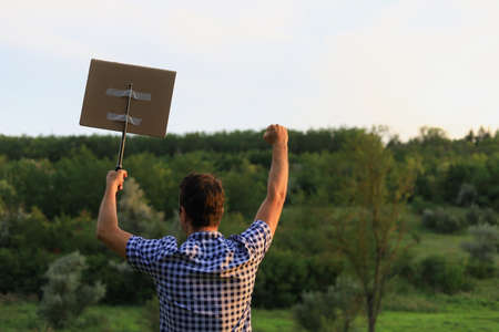 White Caucasian young man or adult guy walks through the park to the city to protest. In his hand he...