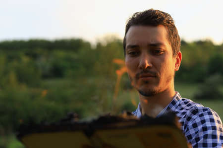 White Caucasian young man or adult guy reading a burning book on blurred forest background.
