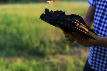 White Caucasian young man or adult guy holds in hands a burning book on blurred forest background.の写真素材