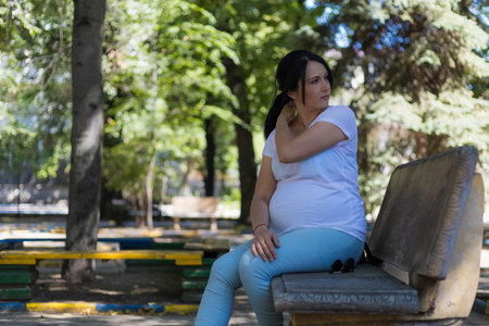 A young pregnant woman in light clothes is resting in the shade of the park's trees on a hot sunny day. Toned background. Selective focusの写真素材