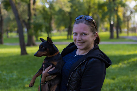 A young woman enjoys companionship with her beloved pinscher dog in a city park. Selective focus with blurred background. Shallow depth of field.の写真素材