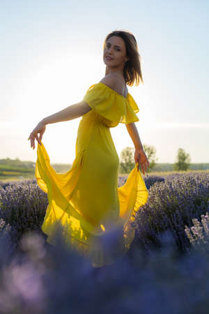 Beautiful and pretty young woman in a yellow dress relaxes and enjoys a walk in the lavender field at sunset, tonedの写真素材
