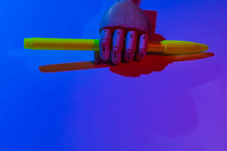 Wooden hand with bright felt-tip pen in neon cyber colors of night street light. Background with...