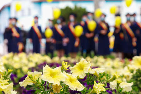 A flower bed with flowers in the foreground and a blurred background with graduates on graduation day. Selective focus background for copy spaceの写真素材