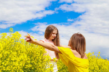 Mom and daughter in nature outdoors lifestyle. Cheerful lightning yellow color of blooming rapeseed field on the background. Happy people concept.の写真素材