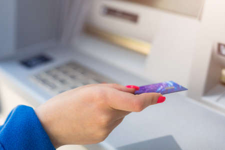 Female hand on a blurred background of an ATM machine with a card. Selective focus. Economics and...