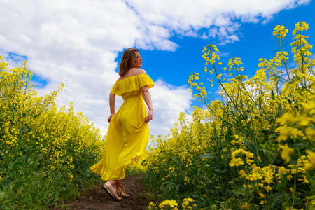 Young pretty woman in yellow dress on lightning cheerful yellow background of blooming rapeseed field. Cheerful yellow lightning conceptの写真素材