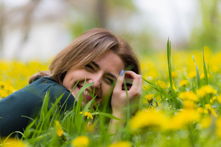 Young woman in a city park during dandelion flowering. Yellow cheerful lightning concept. Symbol of...