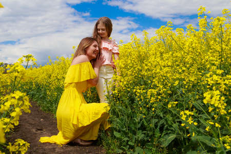 Mom and daughter in nature outdoors lifestyle. Cheerful lightning yellow color of blooming rapeseed field on the background. The concept of unity with nature.の写真素材