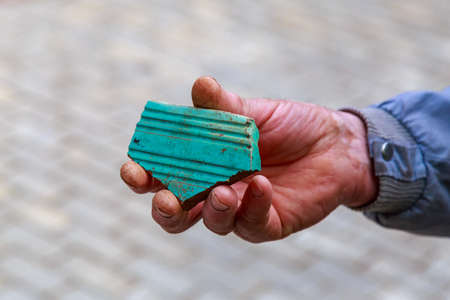 A fragment of an old tile in a mans hand. Roof repair. Background with copy space for text