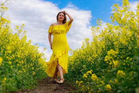 Young pretty woman in yellow dress on lightning cheerful yellow background of blooming rapeseed field. Inspiration conceptの写真素材