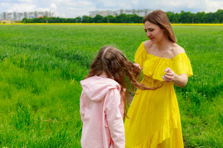 Mom and daughter in nature outdoors lifestyle. Cheerful lightning yellow color of blooming rapeseed field on the background. Maternal love concept.の写真素材