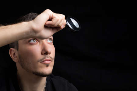 Young handsome man and a magnifying glass on a black background in low key. Search symbol....