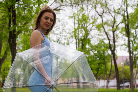 Young woman with transparent umbrella on blurred background of city park. Copy space for textの写真素材