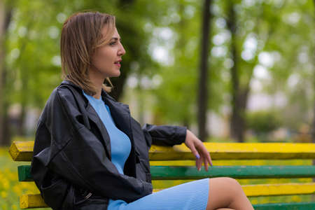 Portrait of a young happy woman of thirty plus years old having a rest in a park sitting on a bench. Copy space for text.の写真素材