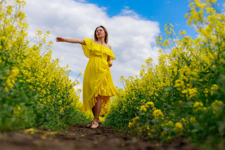 Young pretty woman in yellow dress on lightning cheerful yellow background of blooming rapeseed...