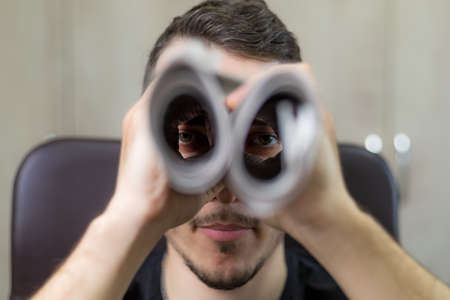 Man holding two twisted roll newspaper. Metaphor or allegory with binoculars. Selective focus on the eyes. Truth search conceptの写真素材
