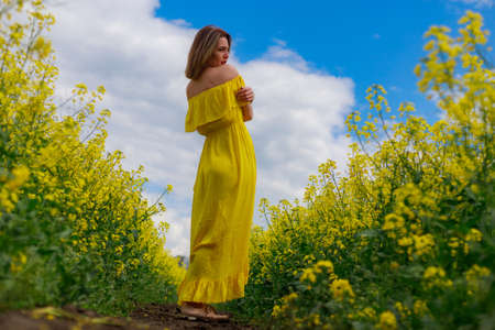 Young pretty woman in yellow dress on lightning cheerful yellow background of blooming rapeseed field. Happiness conceptの写真素材