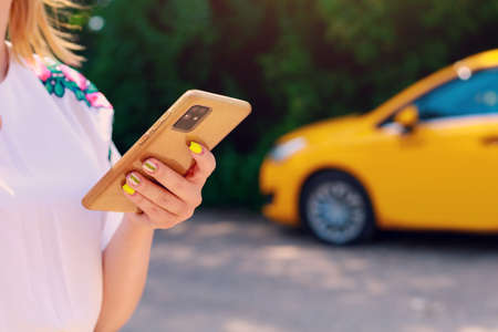Smartphone or phone in female hands on a blurred background of a yellow taxi service car. Car call and control in the application.の写真素材