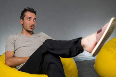 A man in home clothes sits on a bag and watches TV. Selective focus with blurred background for copy space.の写真素材