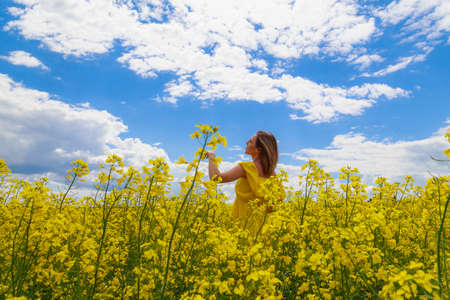 Young pretty woman in yellow dress on lightning cheerful yellow background of blooming rapeseed field. Freedom conceptの写真素材