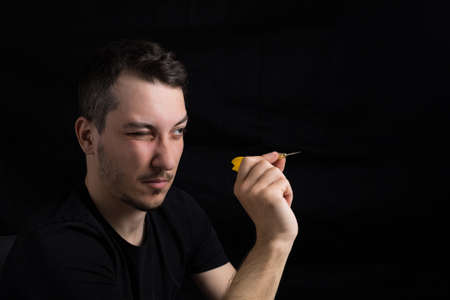 Young handsome man in black clothes with a red dart close-up on a black background in low key. Goal setting conceptの写真素材