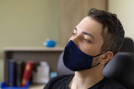 Young handsome man sitting in the office at the table in a mask, lifestyle.の写真素材