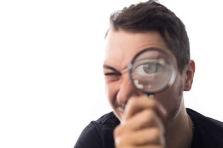 Handsome young man with magnifier, selective focus on eyes. Portrait on a white background.の写真素材