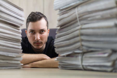 Close up portrait of a young journalist and a stacks of newspapers in a blurred foreground.の写真素材