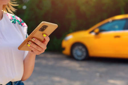 Smartphone or phone in female hands on a blurred background of a yellow taxi service car. Car call and control in the application.の写真素材