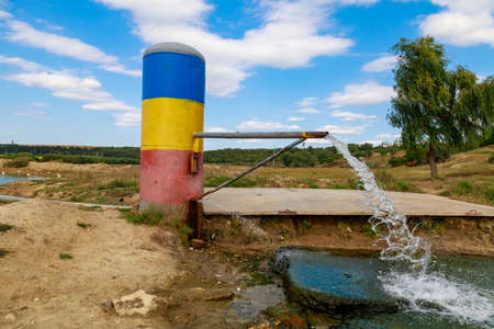 Thermal natural springs of mineral water in the village of Goteshty, Cantemir region, welcome to Moldova. The pipe is painted in the colors of the national flag. Background with copy spaceの写真素材