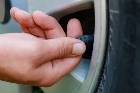 The hand twists or unscrews the nipple cap from the car wheel. Place the air replenishment tires. Toned background with copy space for text or lettering.の写真素材