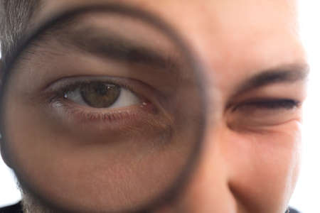 Handsome young man with magnifier, selective focus on eyes. Portrait on a white background.の写真素材