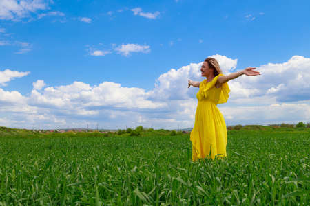 Young woman in a yellow dress outdoors in a green field. The concept of love of life and openness to the worldの写真素材